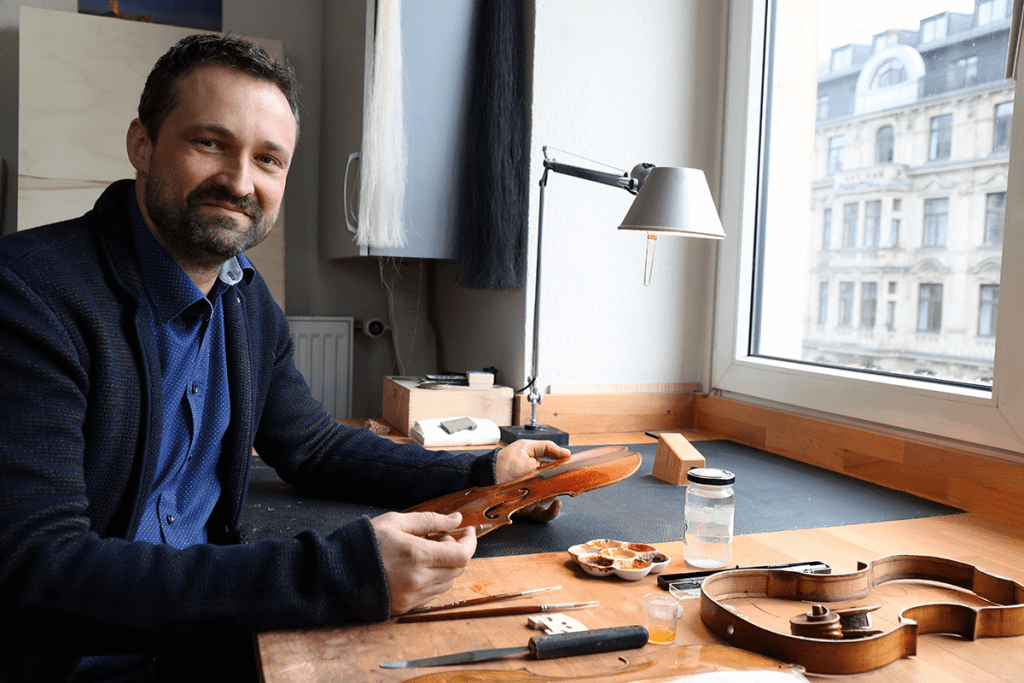 van der Heyd | Geigenbaumeister an der Werkbank blickt in die Kamera